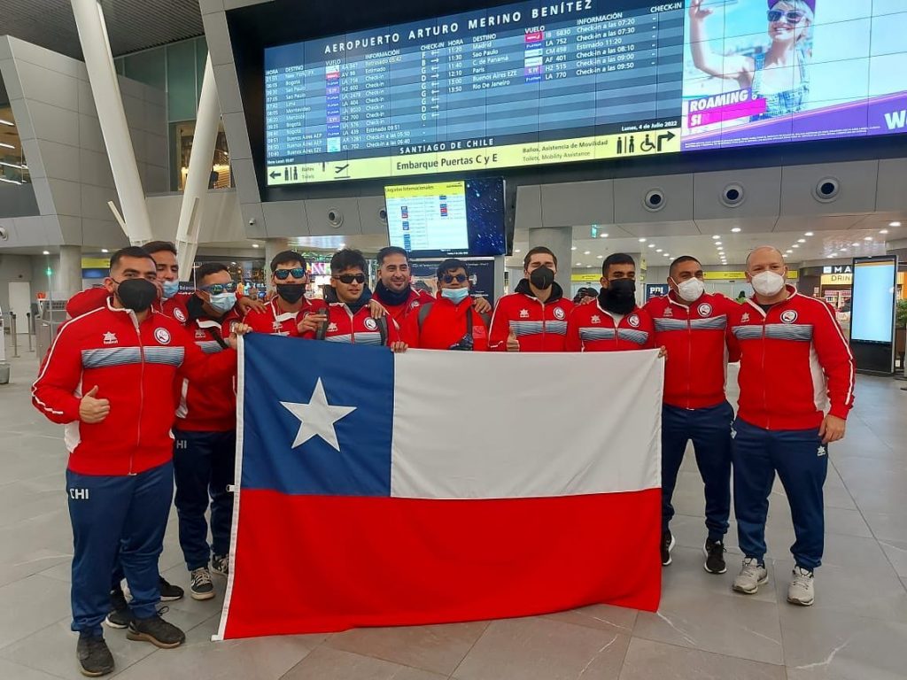 Selección chilena perfilada en el aeropuerto de Santiago minutos antes de la salida internacional. Toda la delegación está uniformada y con la bandera de Chile abierta en el medio.